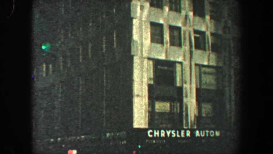 New York City building facade with Chrysler Automobiles signage and dim street detail in 1960 home-movie footage.