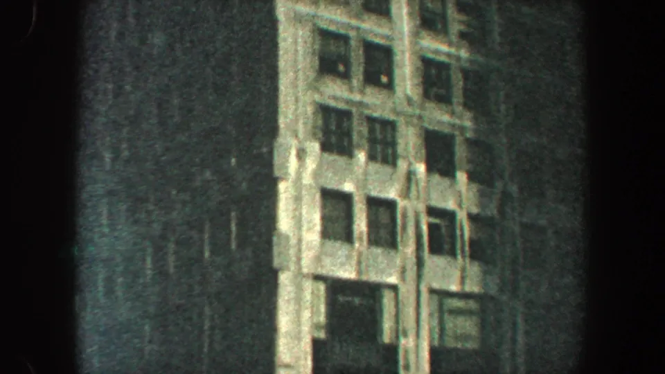 1960 New York City 8mm frame showing the lower portion of a tall Art Deco-style skyscraper facade from a steep street-level angle.