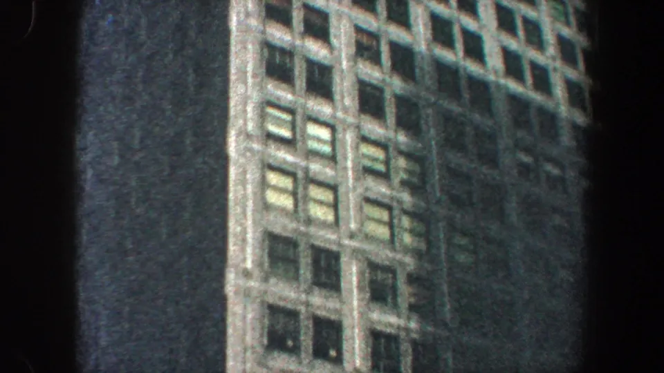 1960 New York City 8mm frame with repeated window bays and vertical facade detailing on a tall skyscraper viewed from below.