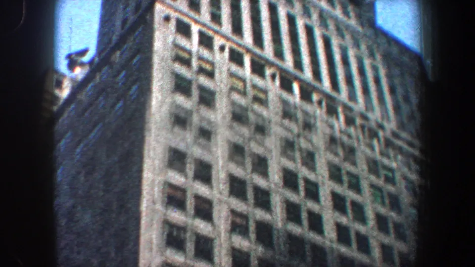 1960 New York City 8mm frame showing a close, upward view of the skyscraper facade with rows of windows and blue sky at the edge.