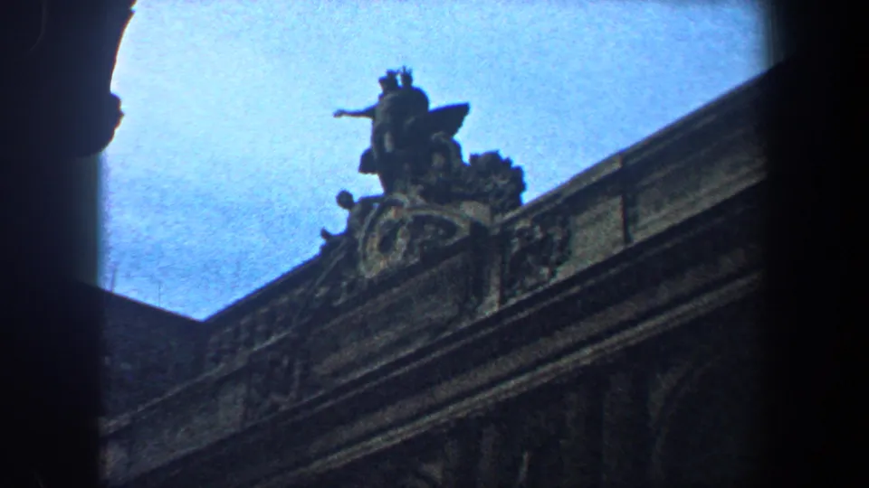 1960 New York City frame showing an ornate rooftop sculpture and cornice silhouetted against blue sky at the end of the pan.