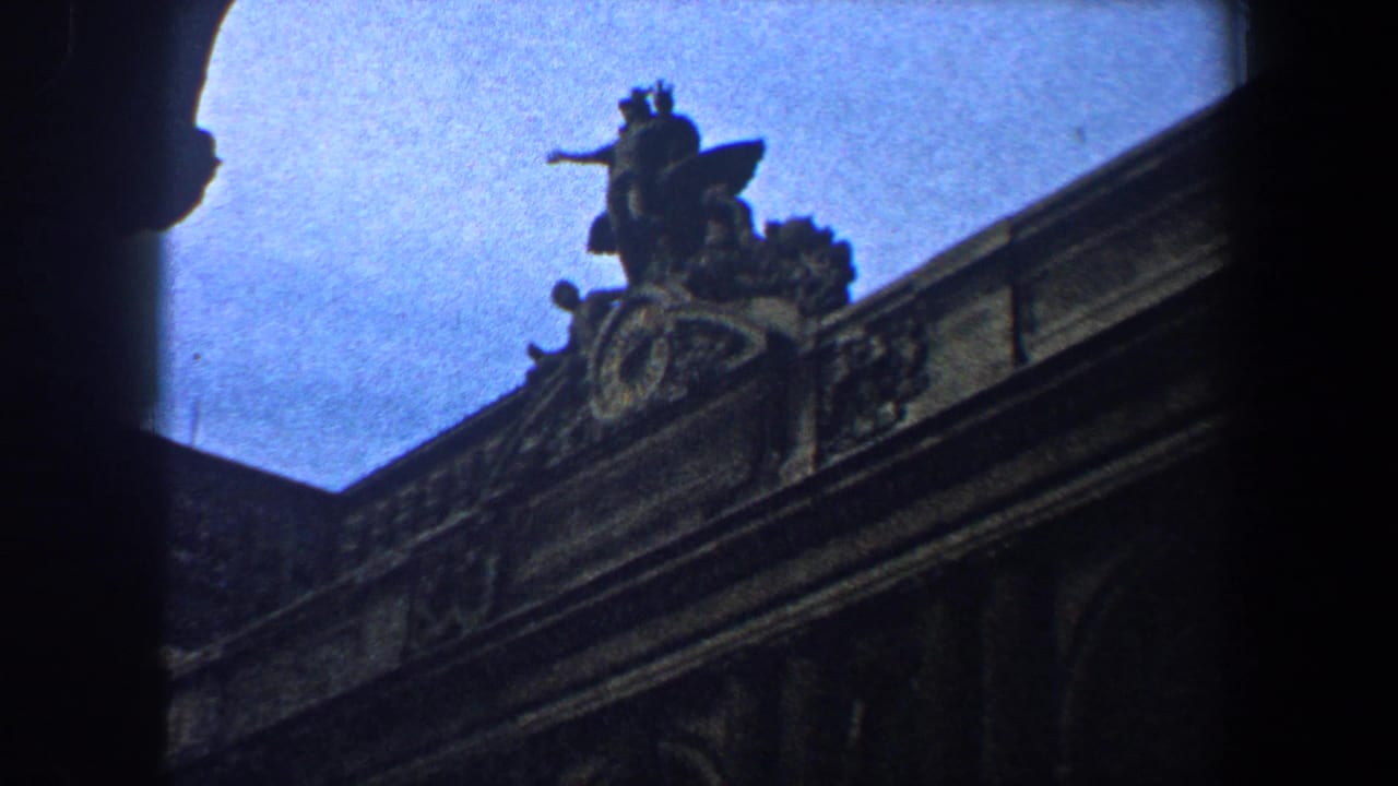 Low-angle view of ornate stone roofline and sculptural figure against a blue sky.