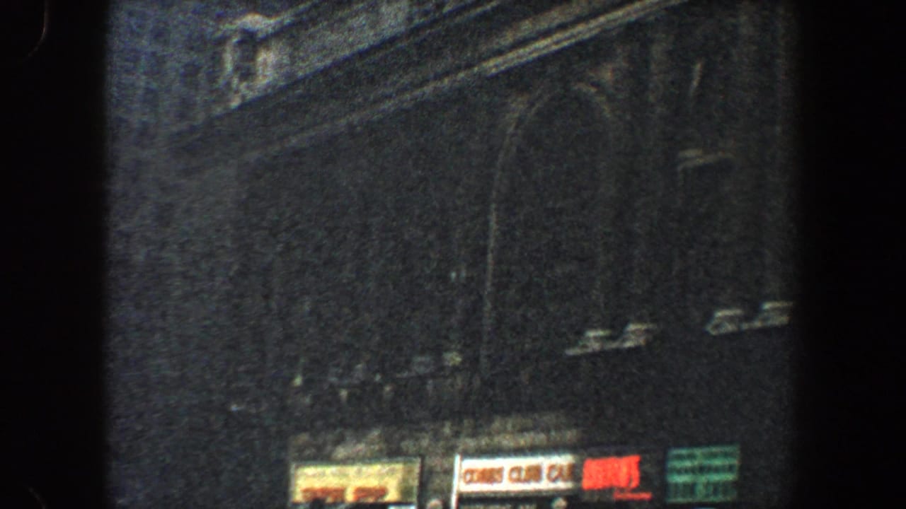 1960 New York City home-movie frame showing a dim ornate facade with arched windows and small street-level signs.