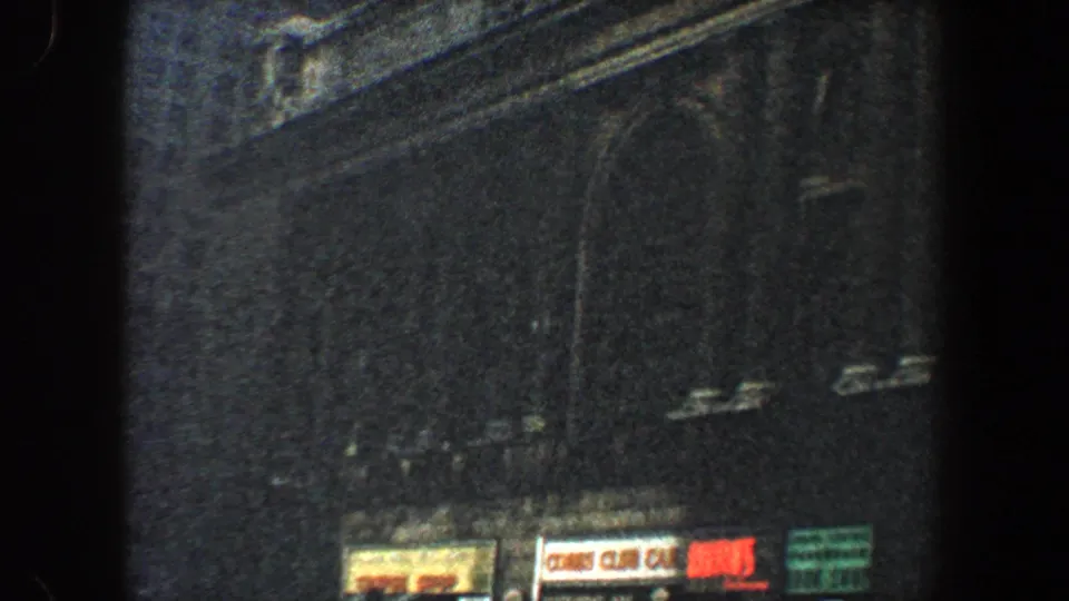 1960 New York City home-movie frame showing a dim ornate facade with arched windows and small street-level signs.