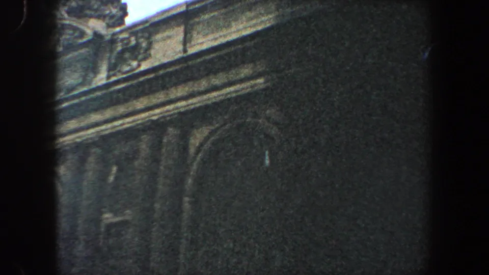 Handheld 8mm frame of an ornate New York City building edge with arched window detail and visible film borders.