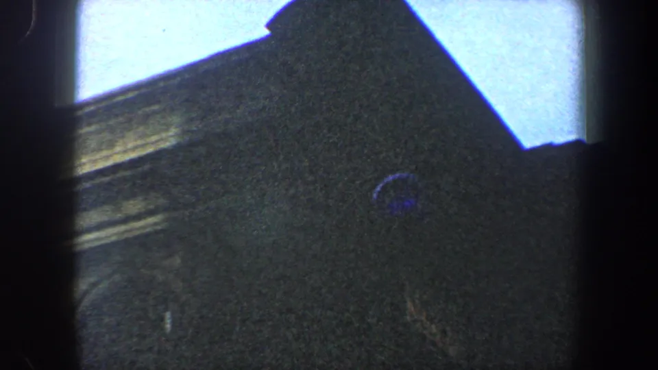 1960 8mm frame of an ornate New York City building facade, with cornice detail, arched forms and blue lens flare.