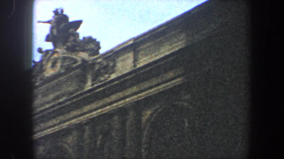 Low-angle 1960 New York City frame showing rooftop ornament, cornice stonework, arched upper windows and bright sky.