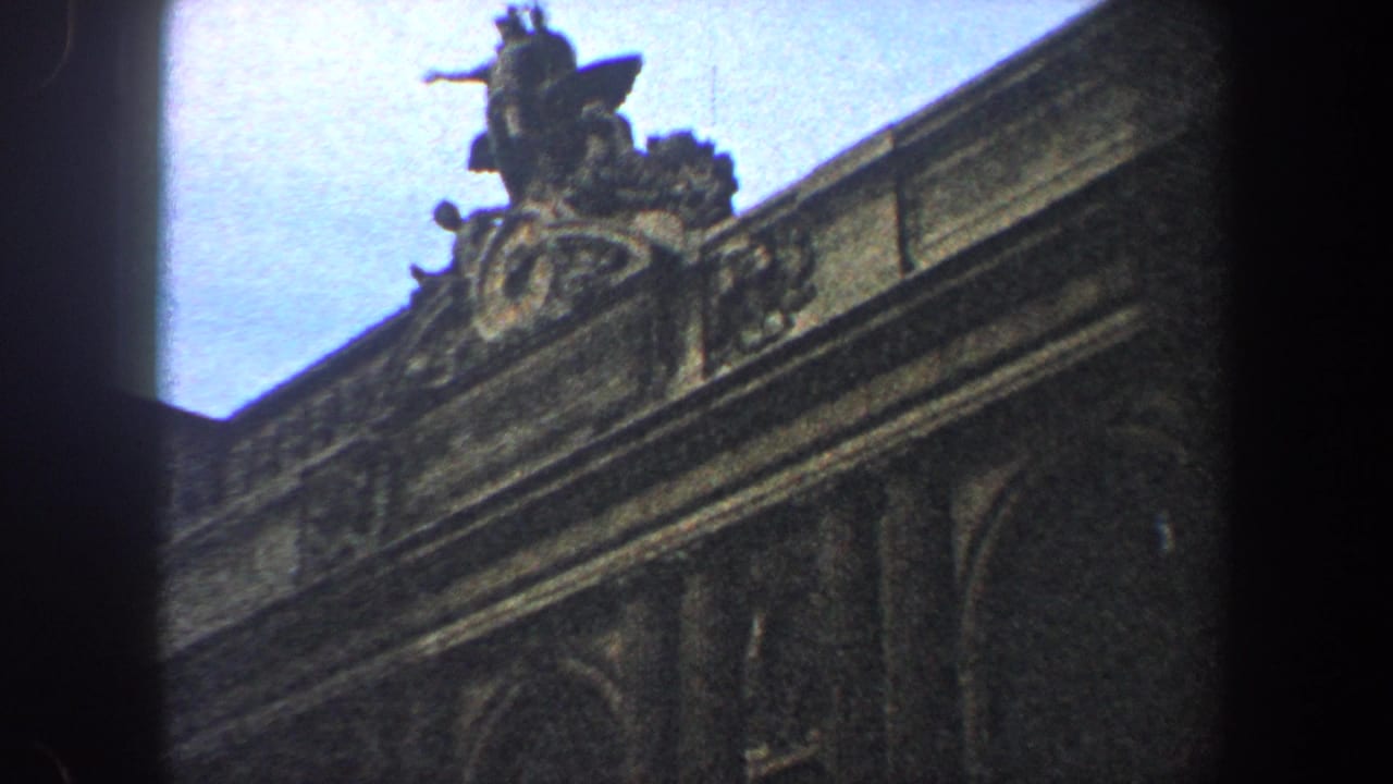 1960 New York City home-movie frame showing an ornate historic building facade with a sculptural figure above the roofline.