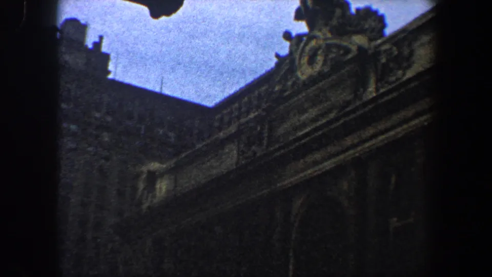 1960 New York City home-movie frame showing a dim, grainy view of ornate stonework and a roof sculpture on a historic building.