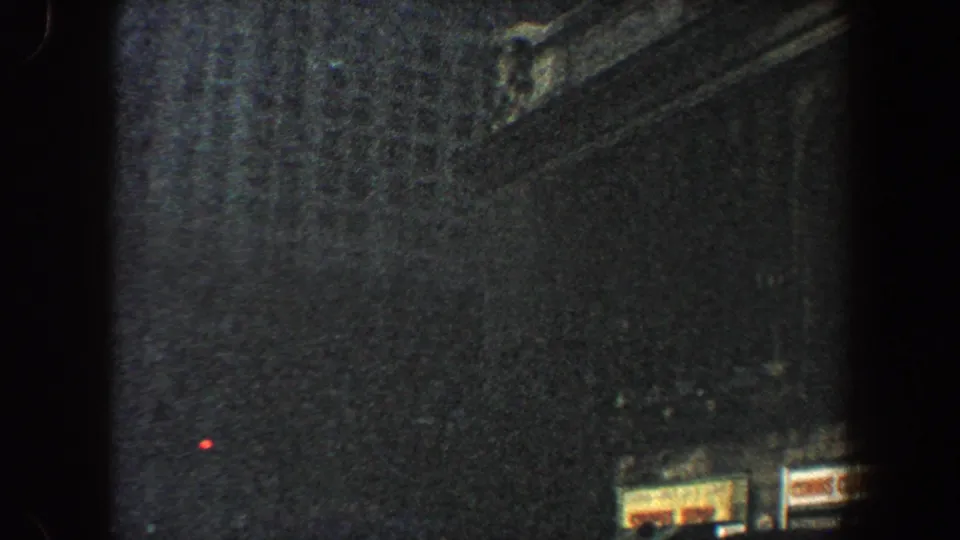 1960 New York City 8mm frame looking up at shadowed skyscraper walls, with small storefront signs near the lower edge.