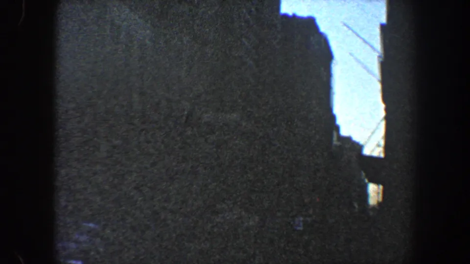 1960 New York City 8mm frame with a dark high-rise silhouette against bright blue sky, seen from street level.