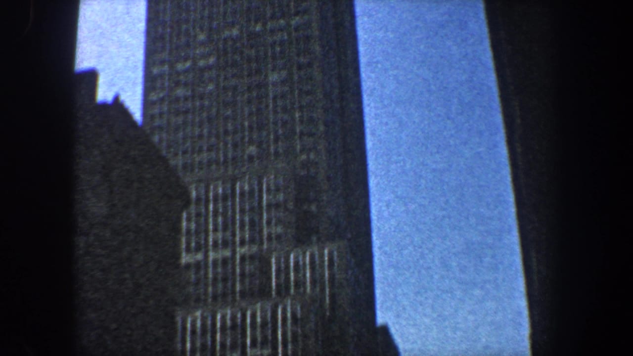 Low-angle view of tall New York skyscrapers with blue sky between dark building edges.