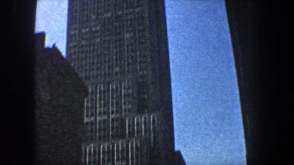 1960 8mm New York City footage shows a low-angle view of skyscraper facades rising against narrow bands of blue sky.