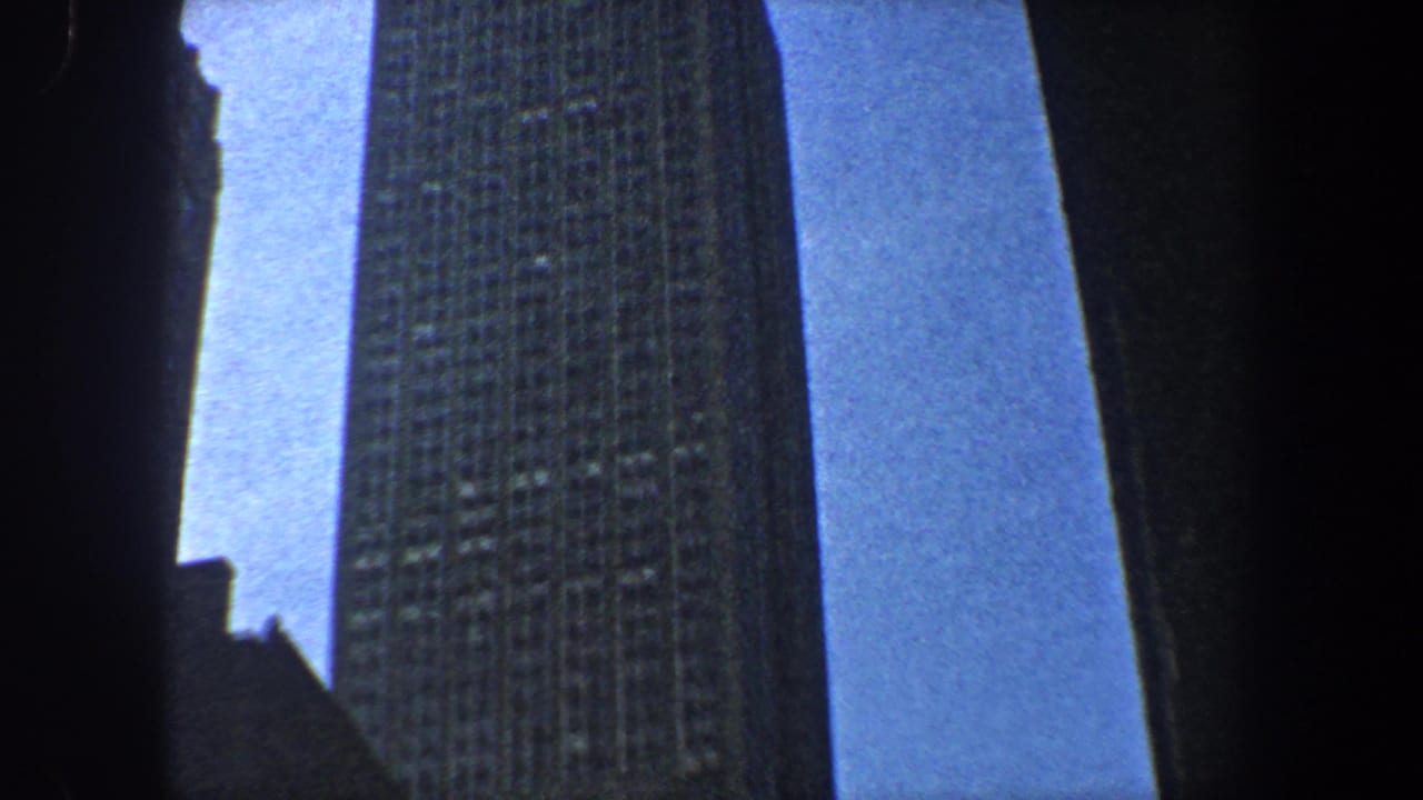 Tall skyscraper facade seen from below, partly framed by dark vertical structures.