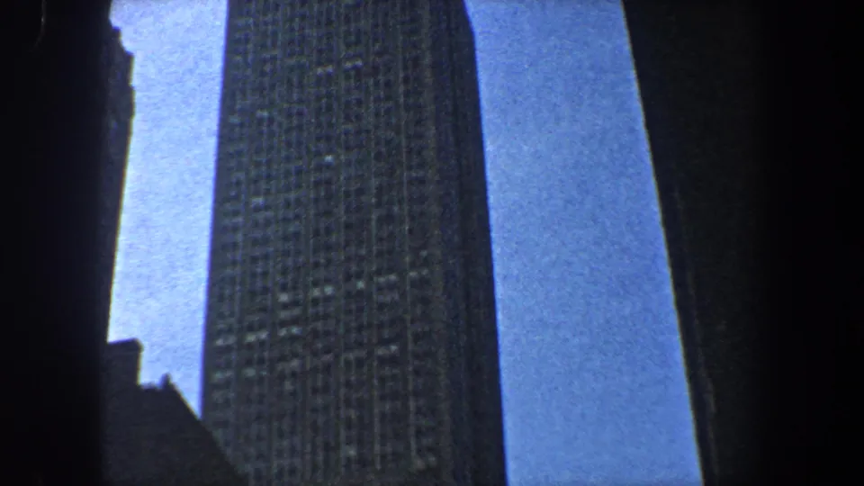 A low-angle 1960 New York City frame shows a gridded skyscraper facade bordered by dark vertical building silhouettes.