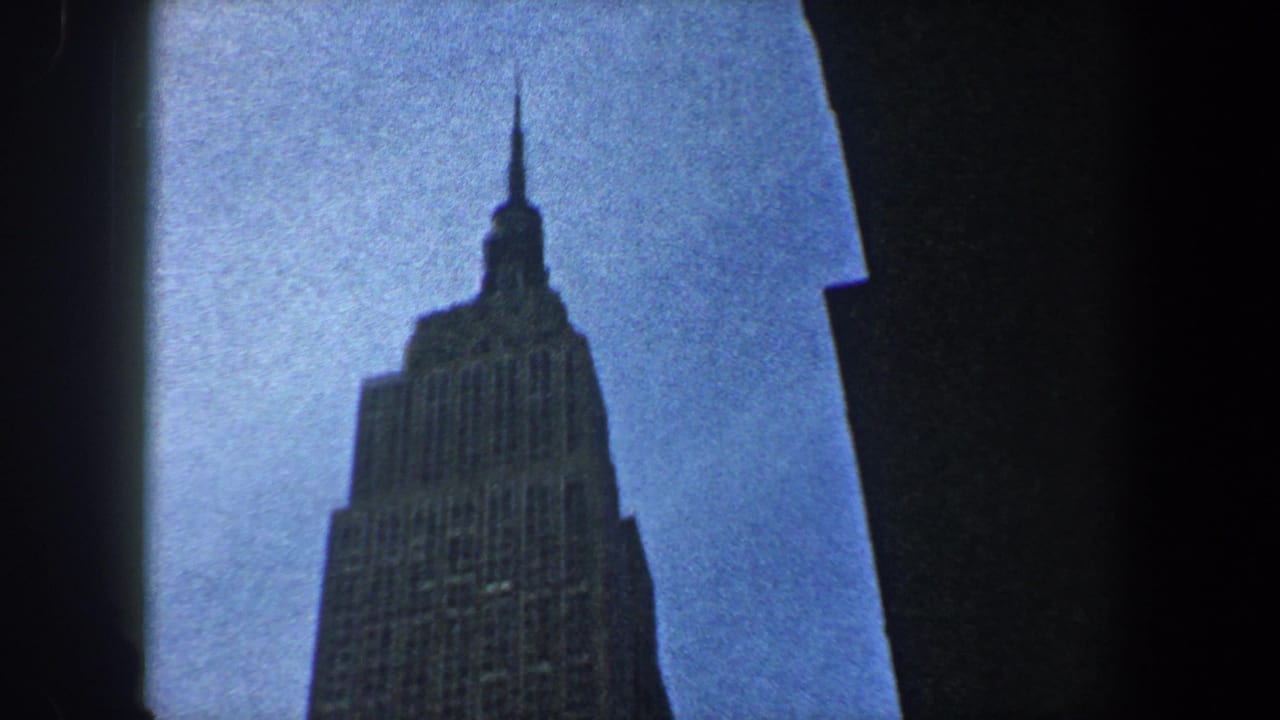1960 New York City 8mm frame looking up at the Empire State Building between dark building edges.