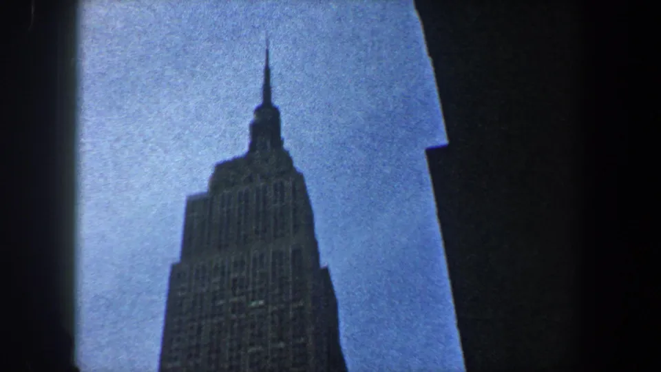 1960 New York City 8mm frame looking up at the Empire State Building between dark building edges.