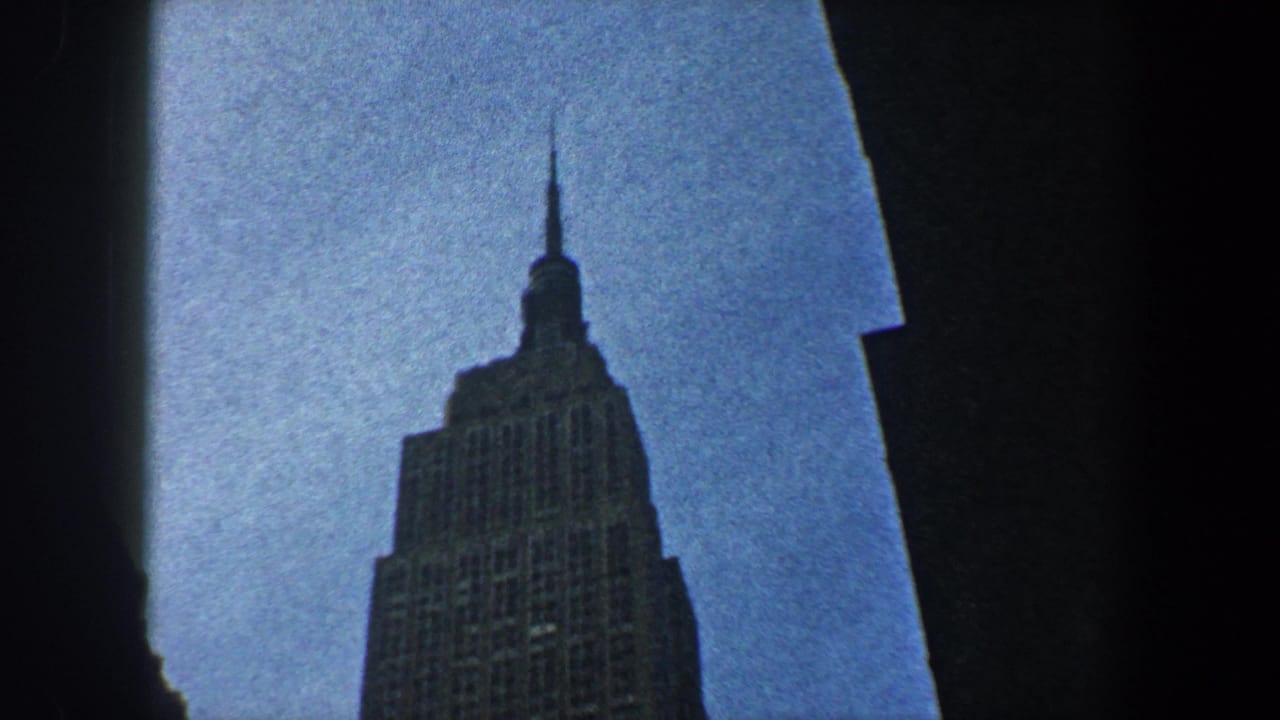 Empire State Building crown framed by dark silhouettes and blue sky.