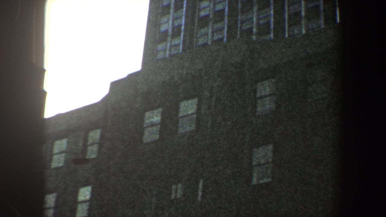 Shadowed upper building facade with windows beside a bright sky opening.