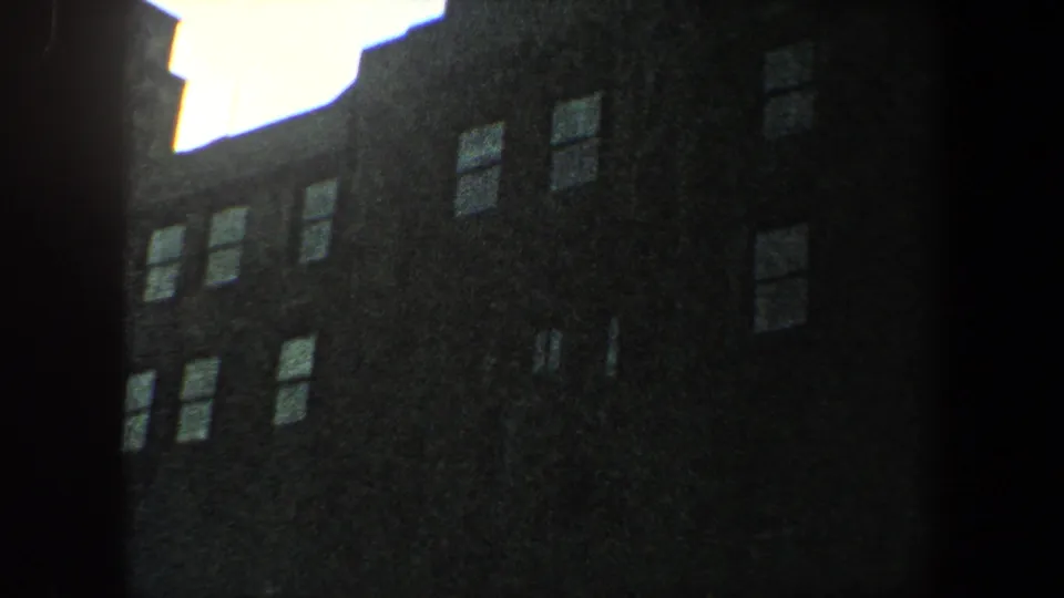 1960 New York City frame showing a shadowed skyscraper face with repeated windows and a bright sky edge above.