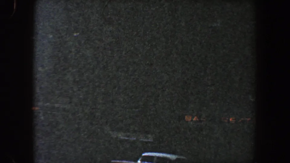 1960 New York City exterior view with a shadowed building facade, dim window shapes, and the top of a vehicle at the bottom of frame.