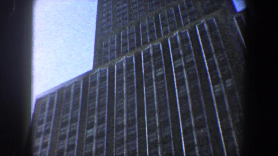Low-angle 1960 New York City frame with the upper stories and corner of a tall skyscraper silhouetted against blue sky.