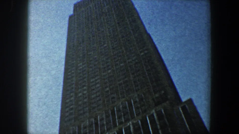 1960 New York City 8mm frame showing the Empire State Building from below with dark film borders and a blue sky.