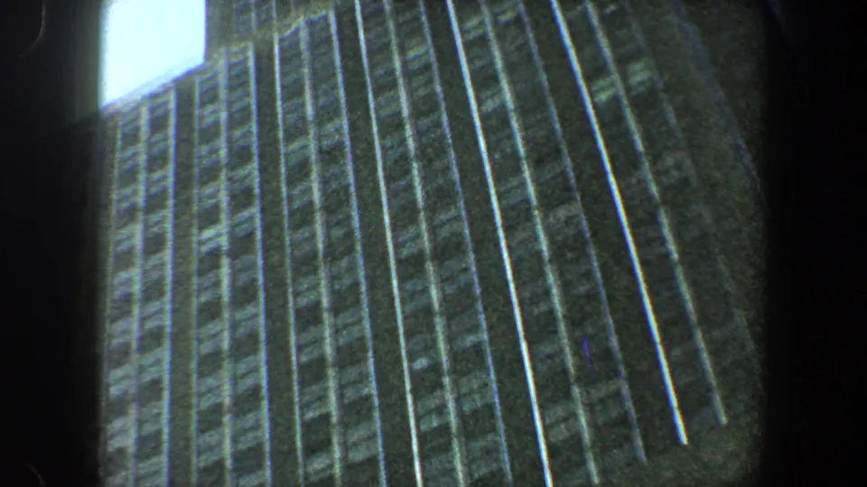 1960 New York City frame showing the Empire State Building facade from below, with visible 8mm grain and heavy edge shadowing.