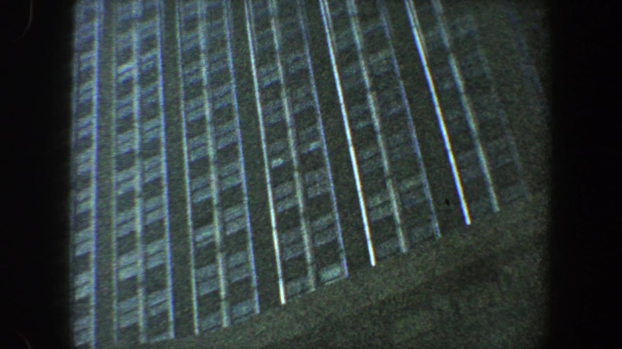 Low-angle view of a tall building facade with rows of windows and dark film edges.