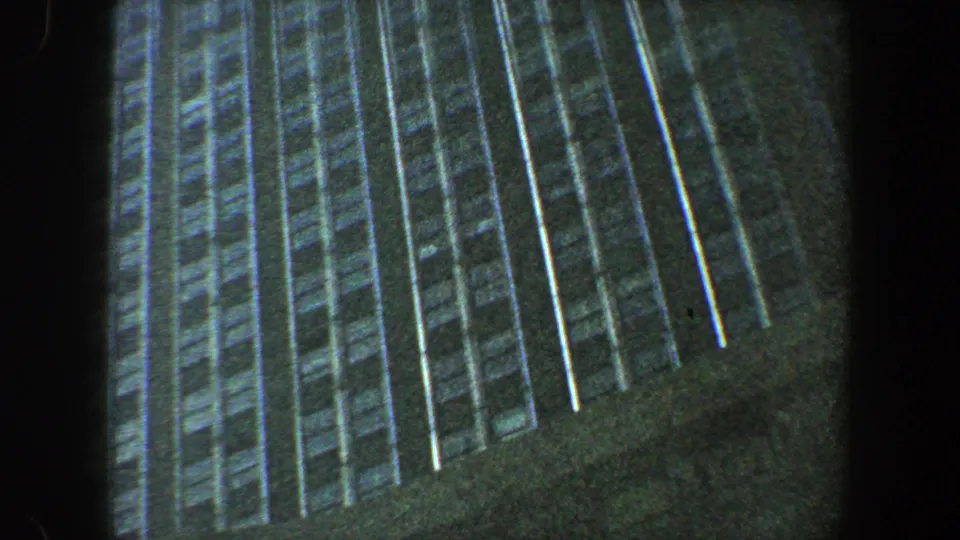 1960 New York City 8mm frame looking sharply upward along a skyscraper facade with repeated windows and deep shadow.