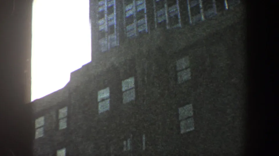 1960 New York City 8mm frame with a low-angle street view of a high-rise edge, window rows, and bright sky.