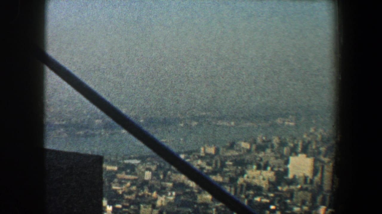 Hazy city skyline seen through dark structural framing and a diagonal bar.