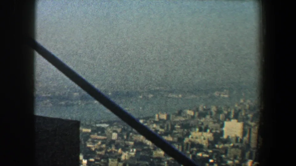 1960 New York City skyline viewed from above through dark framing, with distant water and soft skyscraper detail.