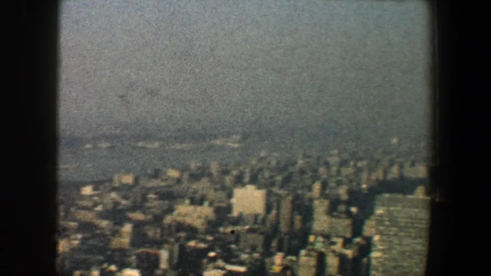 Elevated 1960 New York City view with dense buildings and a distant waterway, divided by dark structural framing.