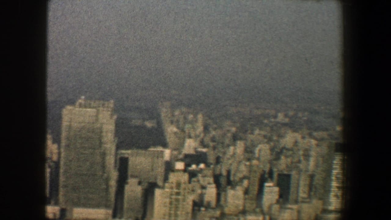 Hazy elevated view of Manhattan towers framed by dark window edges.