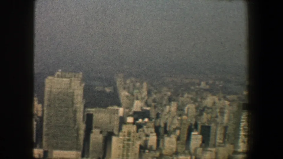 1960 New York City skyline seen from a high vantage point, with skyscrapers softened by haze and dark structural edges in frame.