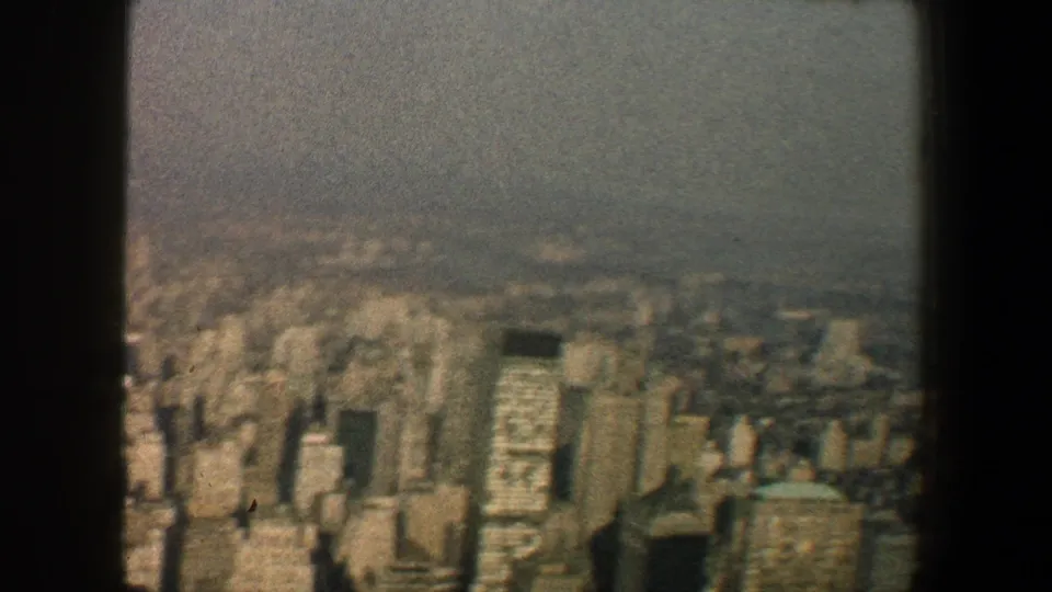Elevated 1960 view across Manhattan buildings, partly divided by a dark vertical beam and softened by grain and haze.