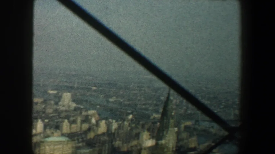 Elevated 1960 New York City view with Manhattan buildings, distant water, and diagonal structural bracing crossing the frame.