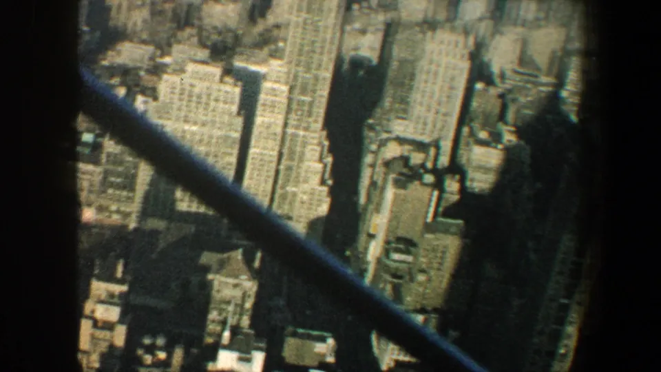 1960 Manhattan skyline and rooftops framed by dark Empire State Building observation-deck crossbars.