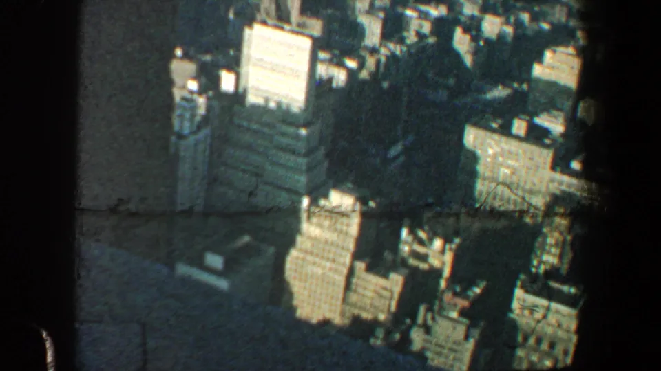 Elevated 1960 New York City view showing waterfront buildings, harbor water, and dark window framing from the observation point.