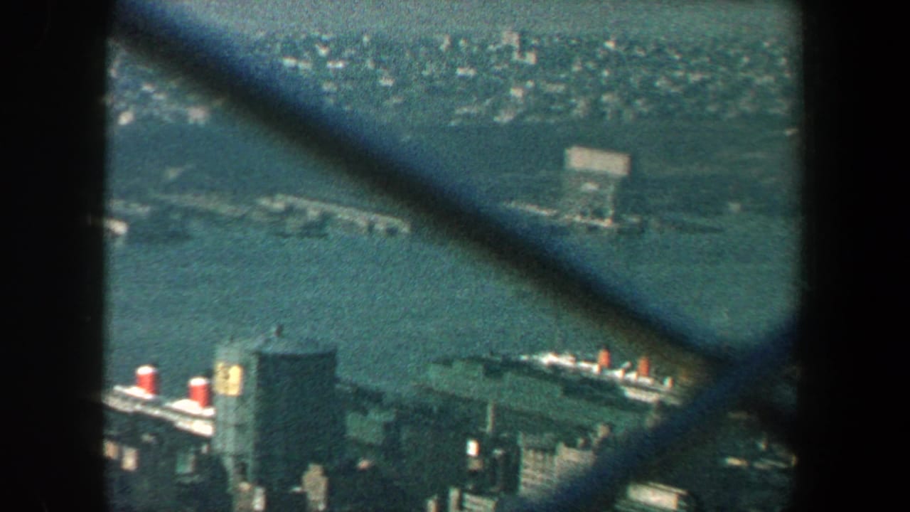 1960 New York City harbor and waterfront buildings filmed through chain-link fencing from a high observation point.
