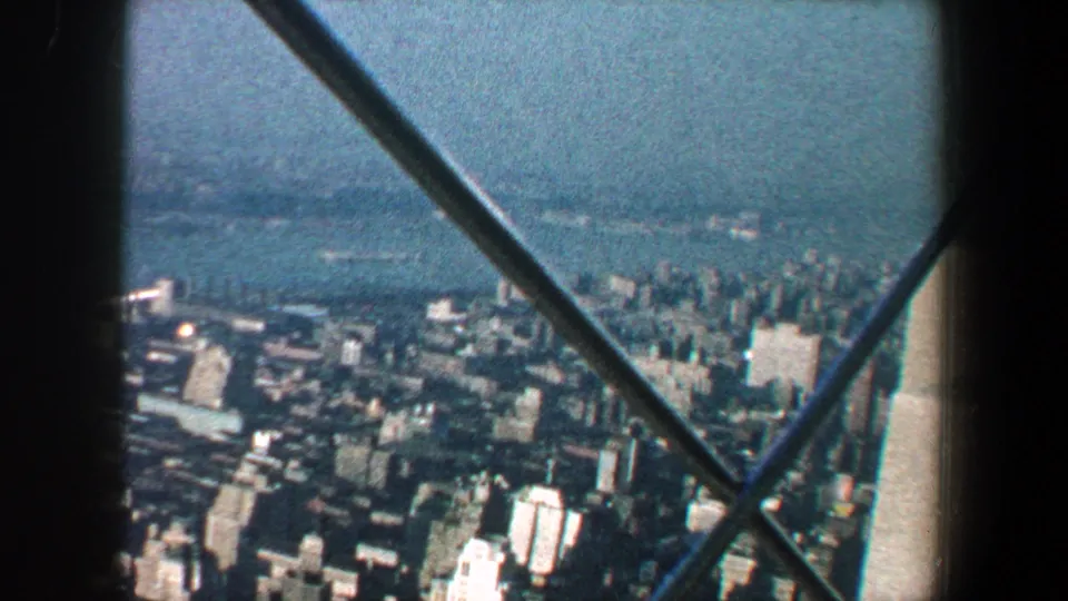 Wide 1960 New York City aerial view across buildings and water, framed by observation-deck fence bars.