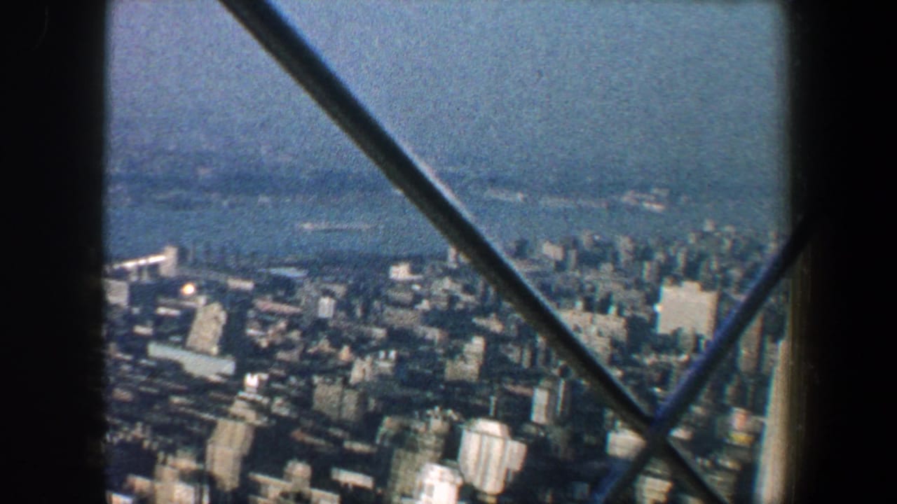 Aerial view of dense city buildings and water seen through dark structural beams.