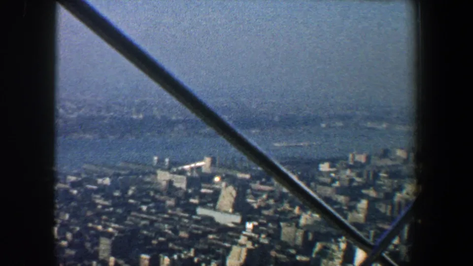 1960 New York City skyline and harbor area viewed from above, with diagonal metal beams crossing the frame.