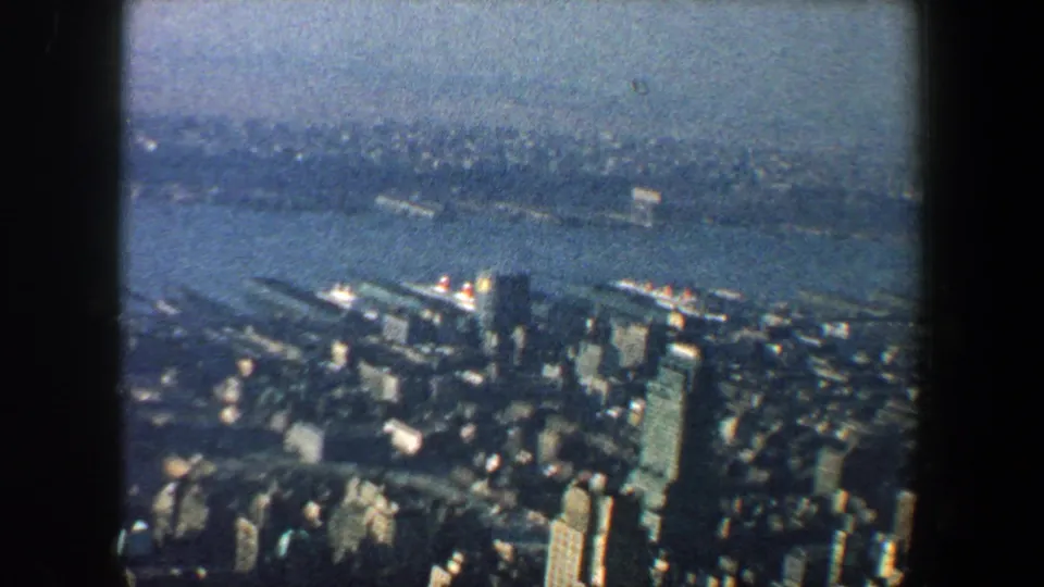 1960 New York City aerial frame showing towers, harbor water, distant skyline, and soft faded 8mm color.
