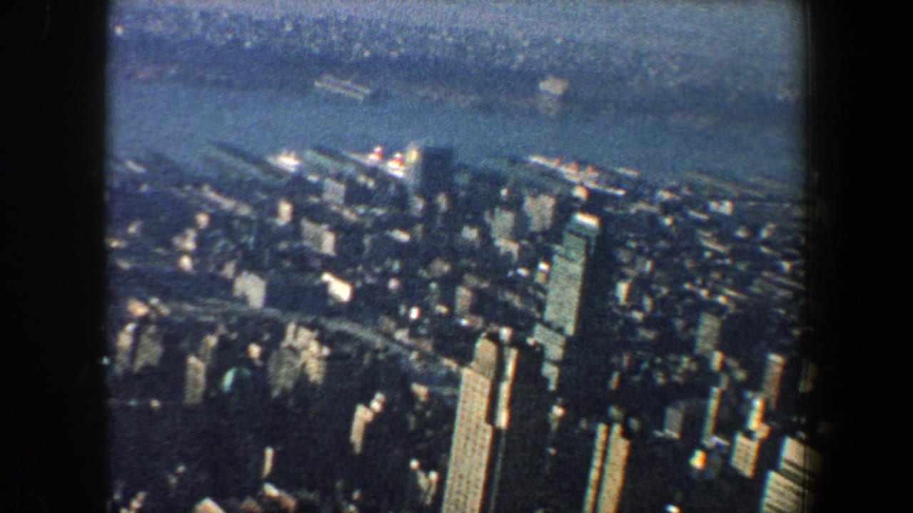 1960 New York City 8mm aerial view looking over dense skyscrapers and the riverfront toward a hazy far shoreline.