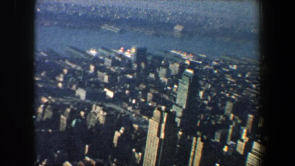 1960 New York City 8mm aerial view looking over dense skyscrapers and the riverfront toward a hazy far shoreline.