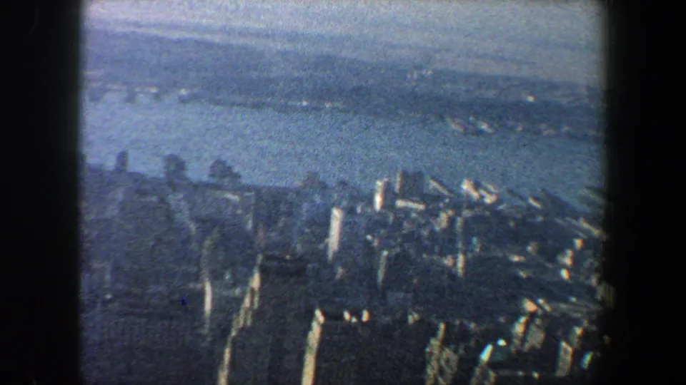 1960 New York City aerial view from 8mm film, with high-rises below, a broad river, and a hazy opposite shoreline.