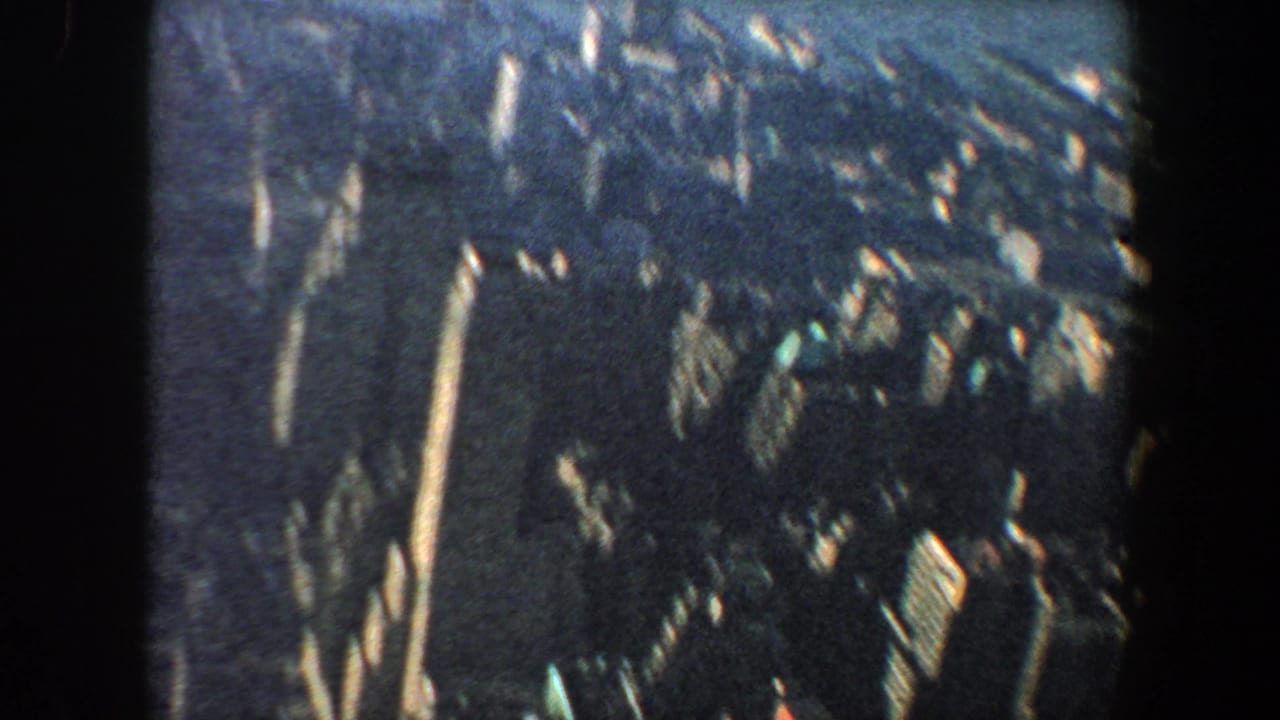 Oblique aerial view of tall city buildings and dense blocks with dark film edges.