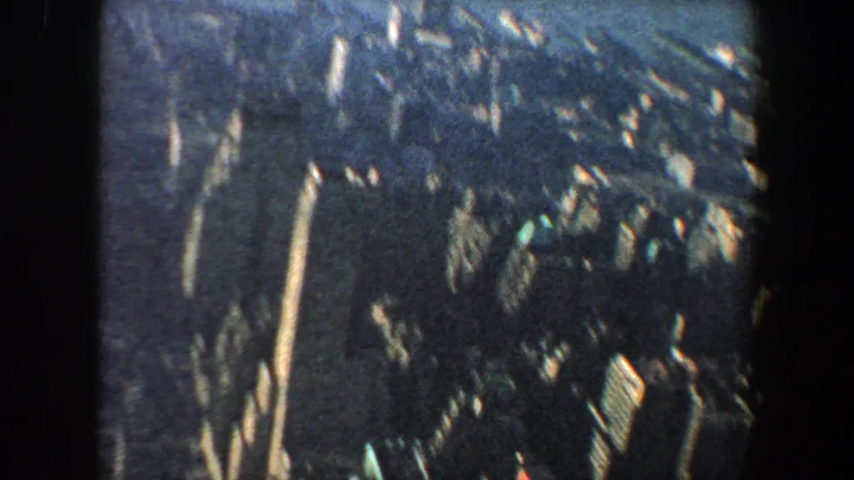 1960 New York City home-movie frame looking down across high-rises and compact urban blocks from an elevated vantage point.